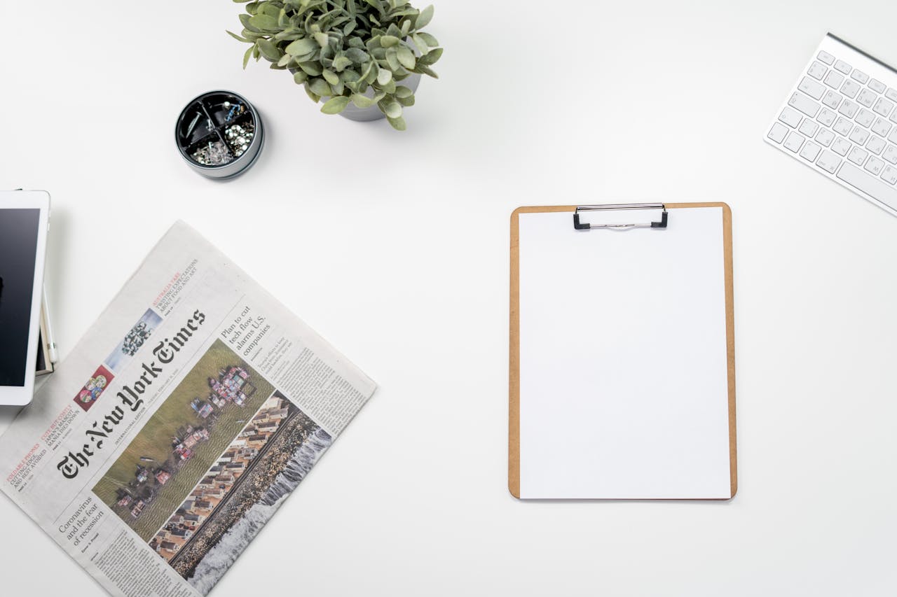Clean flatlay of a home office desk with The New York Times, clipboard, and keyboard.
